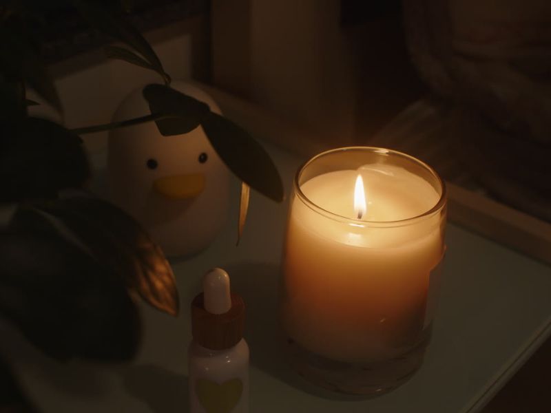 mirisna sveća na noćnom stolčiću pored lampe u obliku pingvina i noćnog seruma